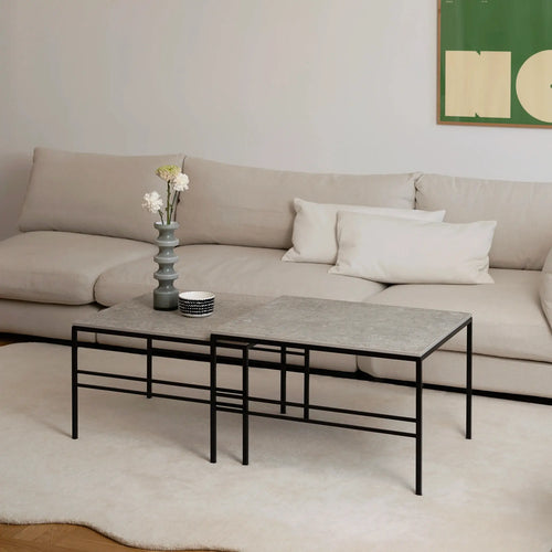 Scandinavian-inspired living room showcasing the Anton Coffee Table 2-set by by Crea in Grigio Dekton with a black frame. The rectangular nesting tables are styled with a sculptural vase and ceramic bowl, positioned in front of a beige modular sofa on a soft cream rug.