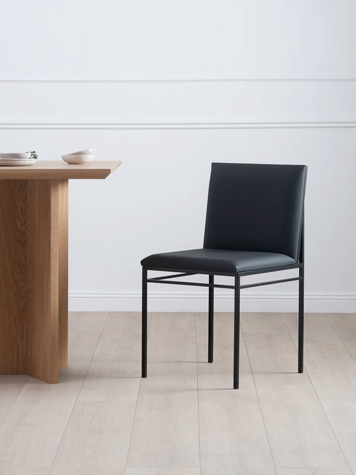 Matstol Bella med svart stativ och Jade Black läder, placerad intill ett matbord i trä.