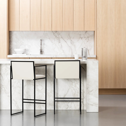 Rear view of two Bruno Bar Stools from by Crea with black steel frames and ivory vegan leather backs, positioned at a white marble kitchen island with natural oak cabinetry.