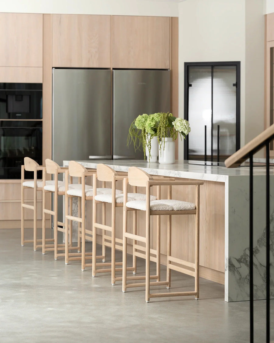 Carl bar stools in natural oak with ivory bouclé cushions, styled at a modern marble kitchen island in a Scandinavian-inspired home.