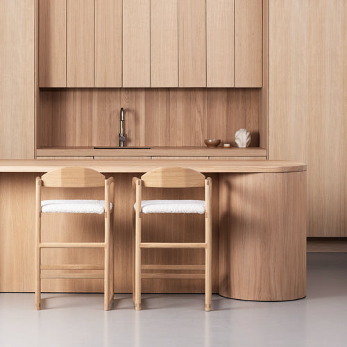 Minimalist oak bar stools with ivory bouclé seats at a wooden kitchen counter, showcasing modern design and soft texture.