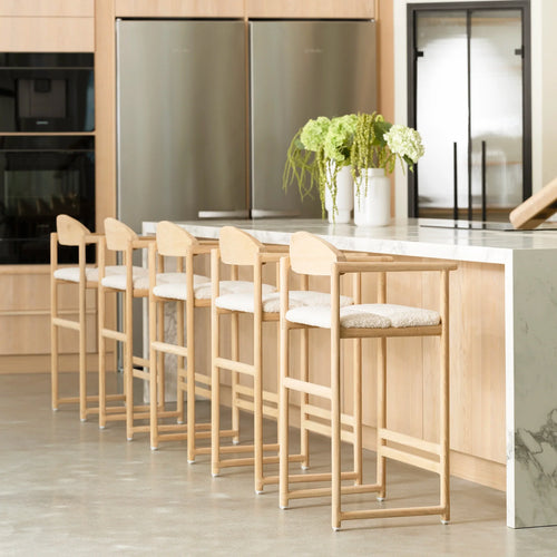 Carl Bar Stools crafted in solid oak with curved backrests and ivory bouclé cushions, styled around a marble kitchen island in a Scandinavian-inspired interior with natural wood cabinetry.