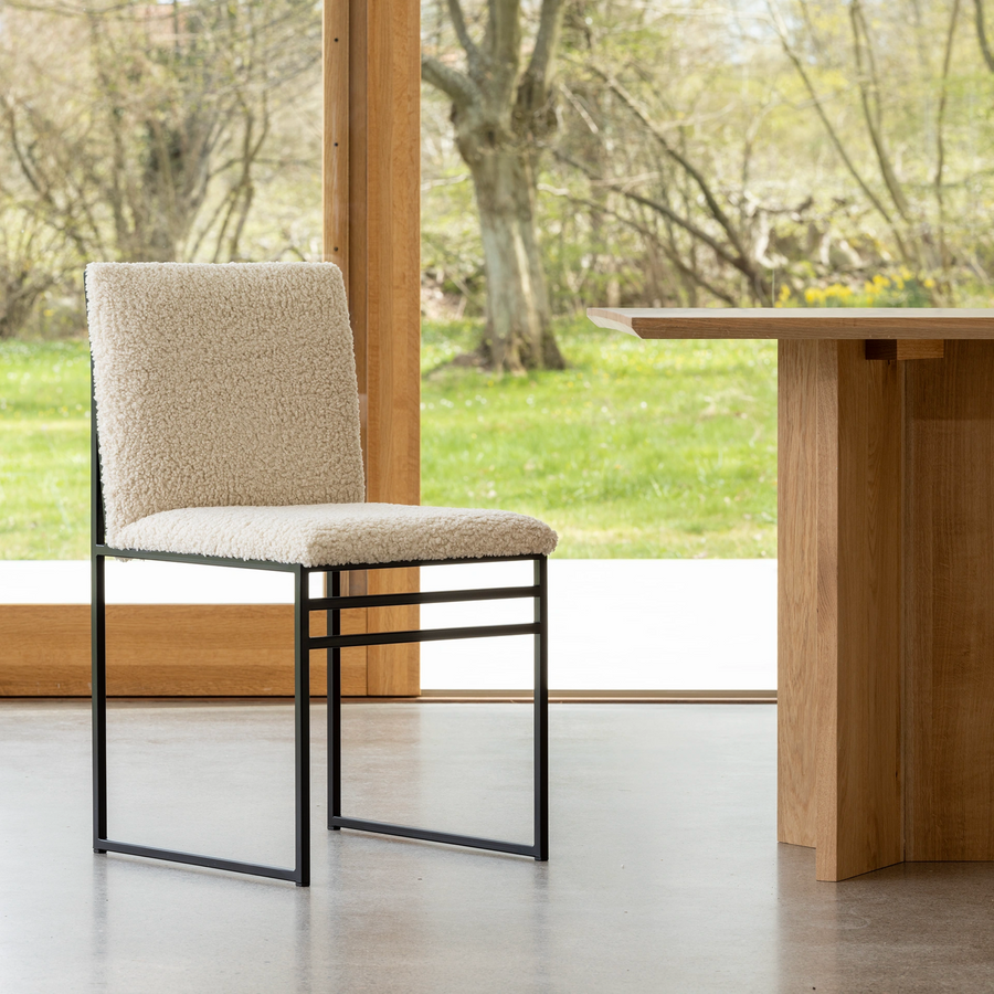 Isabell dining chair in black frame with ivory bouclé upholstery, styled with a solid oak table in a bright room overlooking a green spring garden.