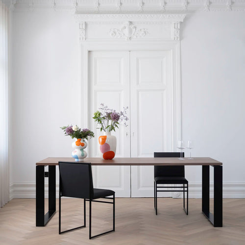 Diana dining table in black with dark oak, minimalistic design, paired with black chairs and decorative vases.