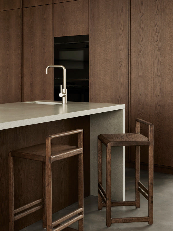 Ebba bar stools in dark-stained solid oak placed by a minimalist kitchen island in a Stockholm archipelago villa.