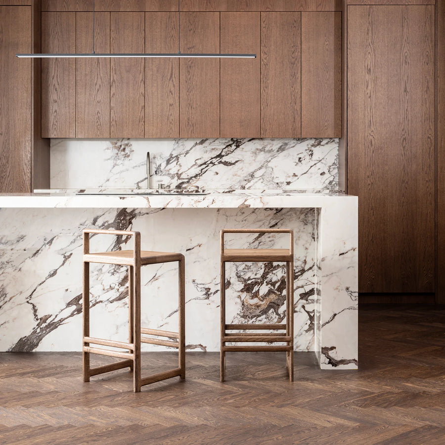 Ebba Bar stool in dark oak featured in a modern kitchen with marble countertop and wooden cabinets.