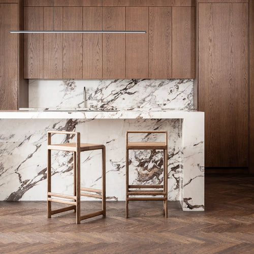 Ebba Bar stool in dark oak featured in a modern kitchen with marble countertop and wooden cabinets.