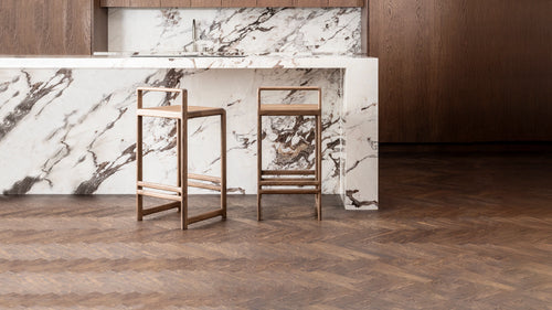 Ebba Bar Stools in dark oak with minimal Scandinavian design, placed at a statement kitchen island in dramatic veined marble, complemented by rich wood cabinetry and herringbone oak flooring.