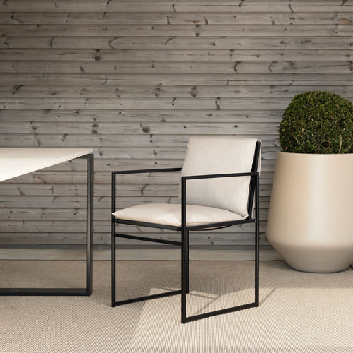 Modern Elsy outdoor chair in black with cushion, set in contemporary outdoor space with green plant.