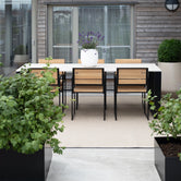 Elsy Outdoor Dining Chairs by by Crea in teak wood and black frame, shown with a white outdoor dining table on a Scandinavian balcony. Custom handmade outdoor furniture, ideal for modern terraces and sustainable living.