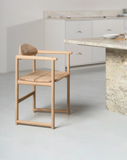 Erik Dining Chair by by Crea in solid oak with armrests, placed beside a stone countertop in a minimalist kitchen interior.