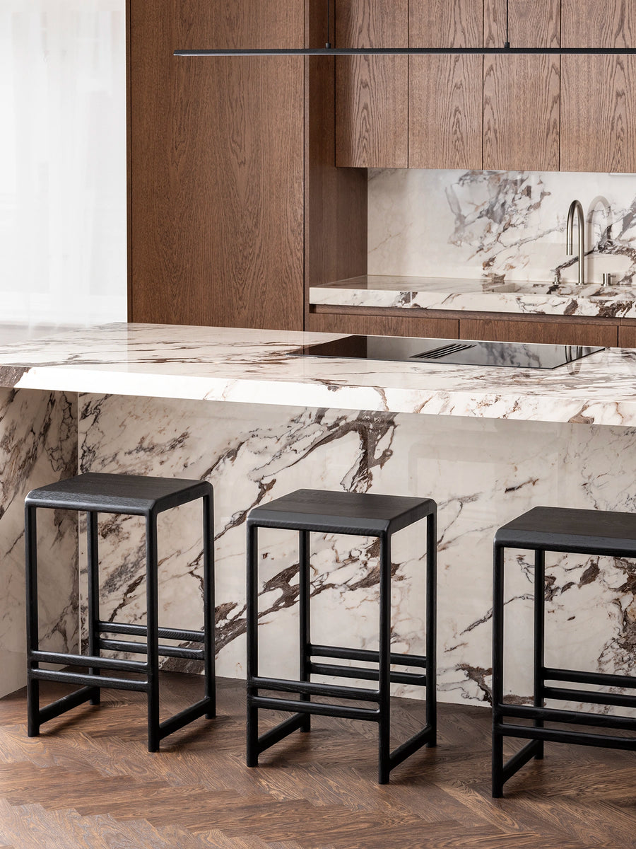 Three black oak bar stools with wood seats at a modern kitchen island with marble countertop.