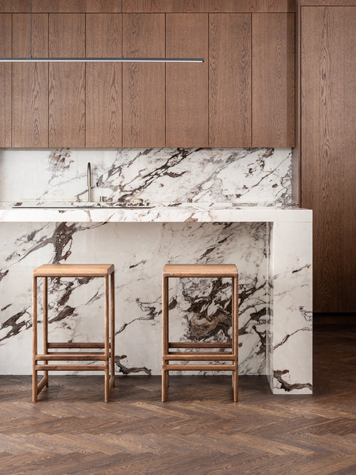 Oak Bar Stool Eva in dark oak at a modern kitchen counter with marble backsplash.