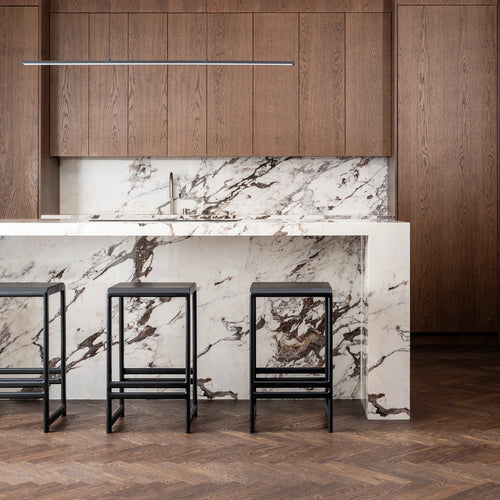Three By Crea Eva bar stools crafted from solid black oak, featuring a minimalist design, set against a luxurious white marble kitchen island and dark wooden cabinetry. Perfect for modern kitchen interiors, high-end furniture showrooms, and sophisticated home decor.