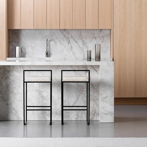 Freja bar stools with black frame and ivory bouclé cushions in modern kitchen with marble countertop.