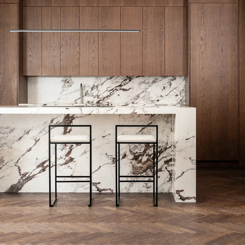 Freja bar stools with ivory leather cushions in modern kitchen with marble countertop and wooden cabinets.