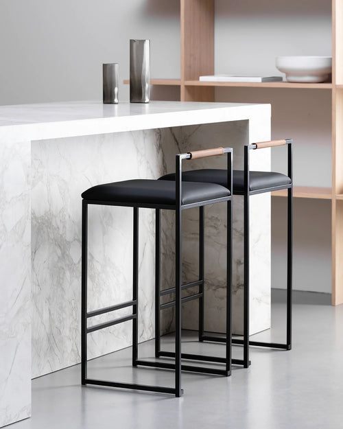 Freja bar stools by by Crea featuring black vegan leather cushions and Coffee Bean wooden backrests, styled at a modern marble kitchen island.