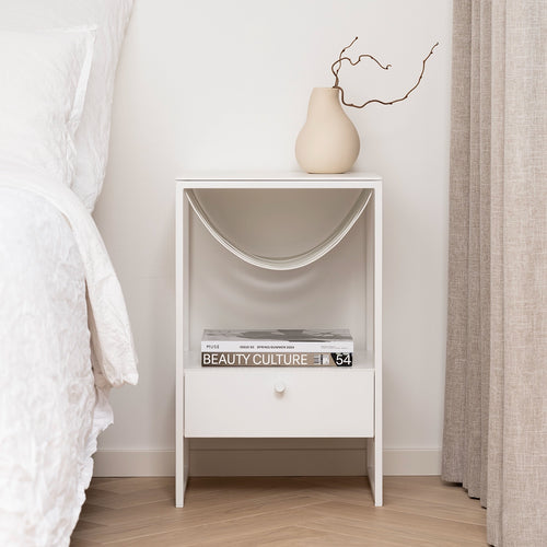 Iris bed table in white with minimalist design, featuring a drawer and decorative vase, ideal for modern interiors.
