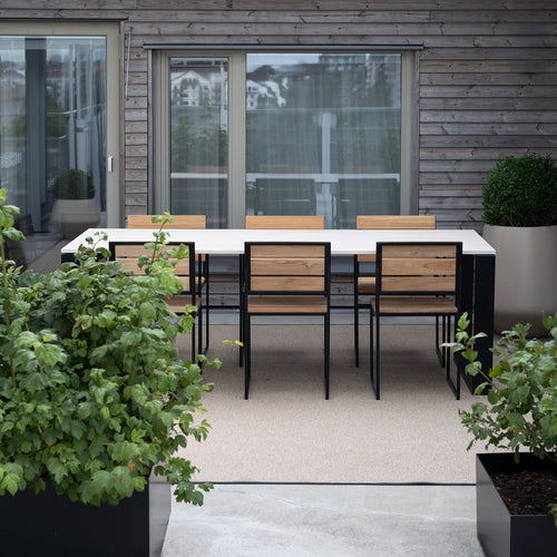 Isa Outdoor Dining Chairs by by Crea in teak and black frame, paired with a minimalist outdoor dining table on a Scandinavian terrace. Exclusive handmade outdoor furniture for modern and sustainable living.