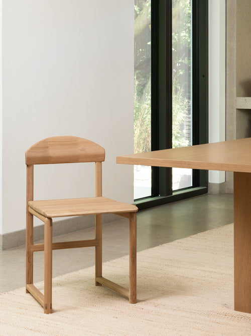 Dining chair Karin in oak wood frame, showcasing sculpted curves and solid design in a modern dining setting.