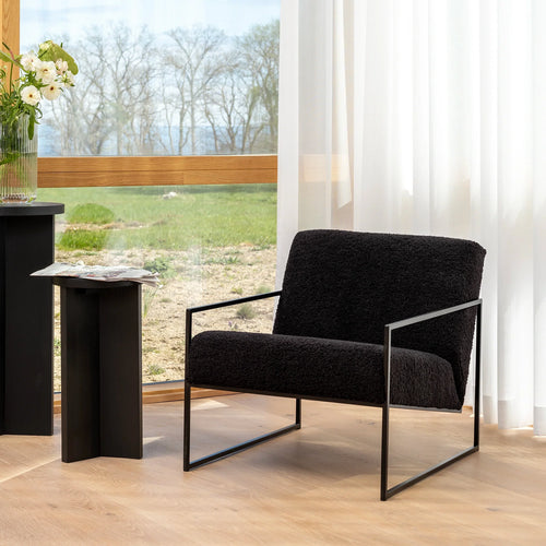 Kent armchair in black bouclé beside a sleek table, showcasing minimalist Scandinavian design in a bright interior.