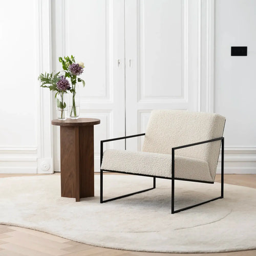 Armchair Kent – Black Frame – Ivory Bouclé Cushion in a minimalist interior setting with a side table and flowers.