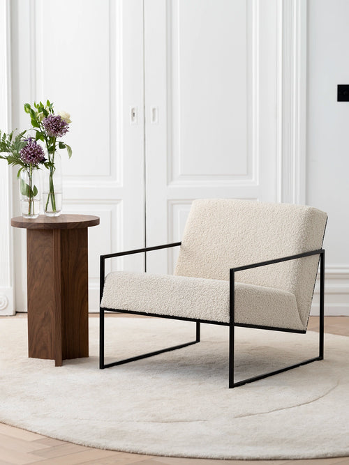 Armchair Kent – Black Frame – Ivory Bouclé Cushion in a minimalist interior setting with a side table and flowers.