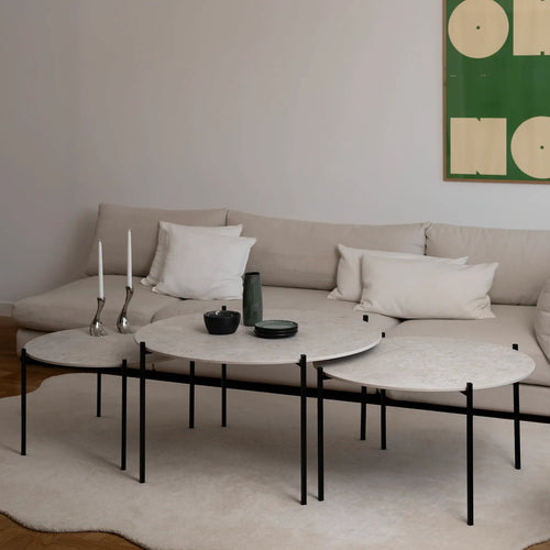 Leo Coffee Table 3-set by by Crea with Sabbia Dekton tops and black steel frames, styled in a Scandinavian living room with a beige sectional, modern green wall art, and candleholders. Handmade exclusive furniture for contemporary interiors.