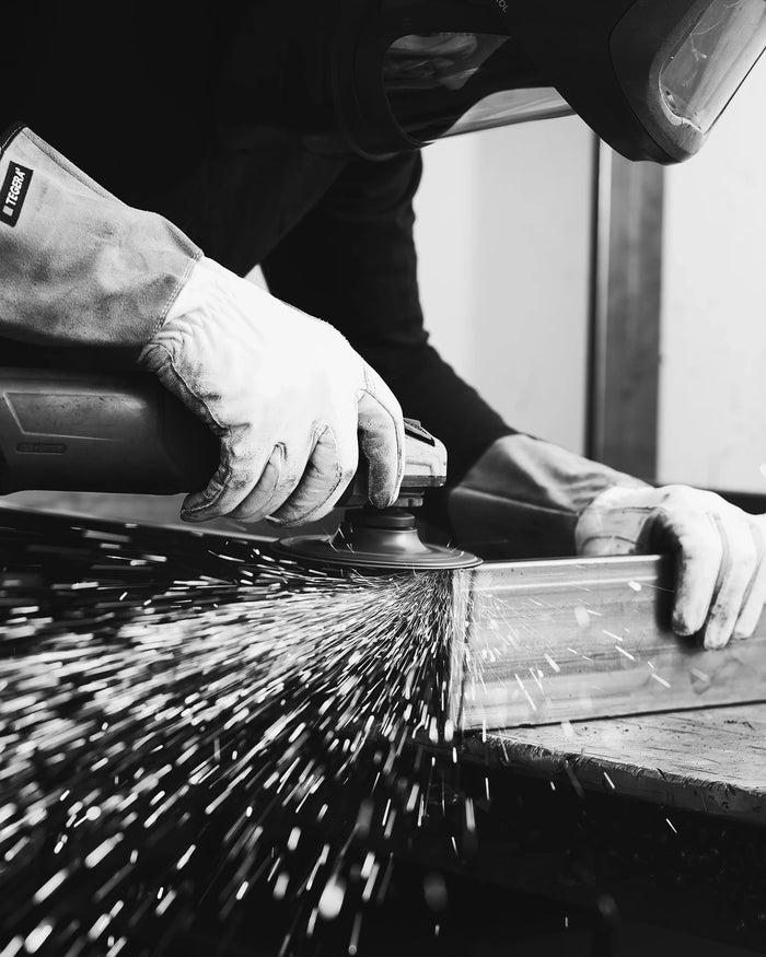 Person using a grinder with sparks flying, wearing protective gloves and a helmet.