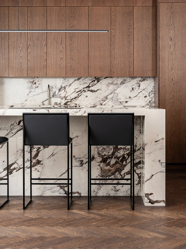 Bar Stool Philip in kitchen with black frame and jade black leather cushion next to marble countertop.