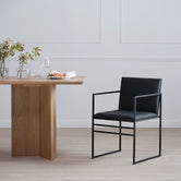Modern dining scene featuring a sleek By Crea Sella chair in black with a minimalist frame, paired with a natural oak dining table, against a classic white wainscoting wall. Ideal for contemporary dining room furniture, Scandinavian design, and stylish home decor