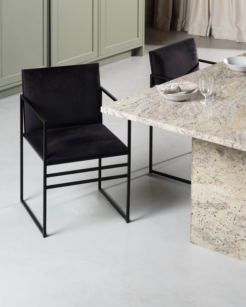 Sella Dining Chair by by Crea in jade black velvet upholstery with minimalist black steel frame, placed by a natural stone kitchen island in a Scandinavian-inspired interior.