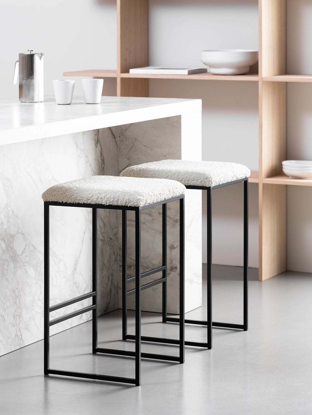 Bar Stool Svea in black with ivory bouclé upholstery, stylishly placed at a modern marble countertop.