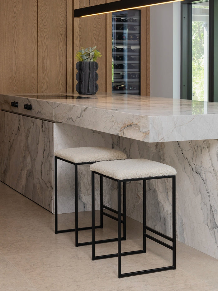 Bar Stool Svea in black with ivory bouclé fabric beside a modern marble kitchen island.