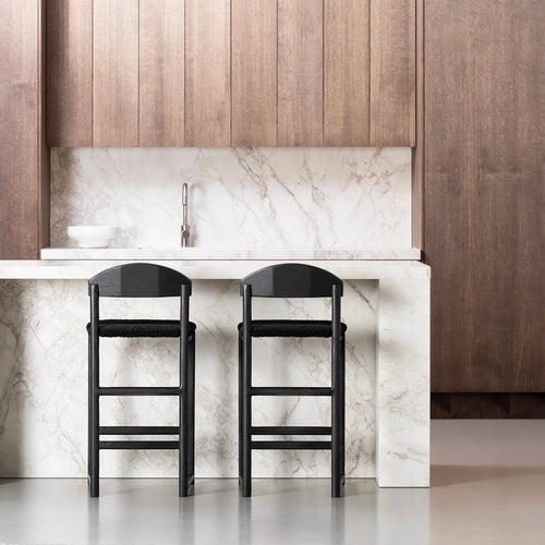 Stylish black oak bar stools with black bouclé seats in modern kitchen setting with marble countertop.