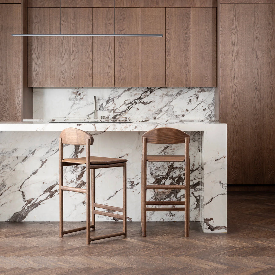 Ted bar stools in dark oak with wooden backrests against a sleek marble kitchen island, showcasing modern Nordic design.