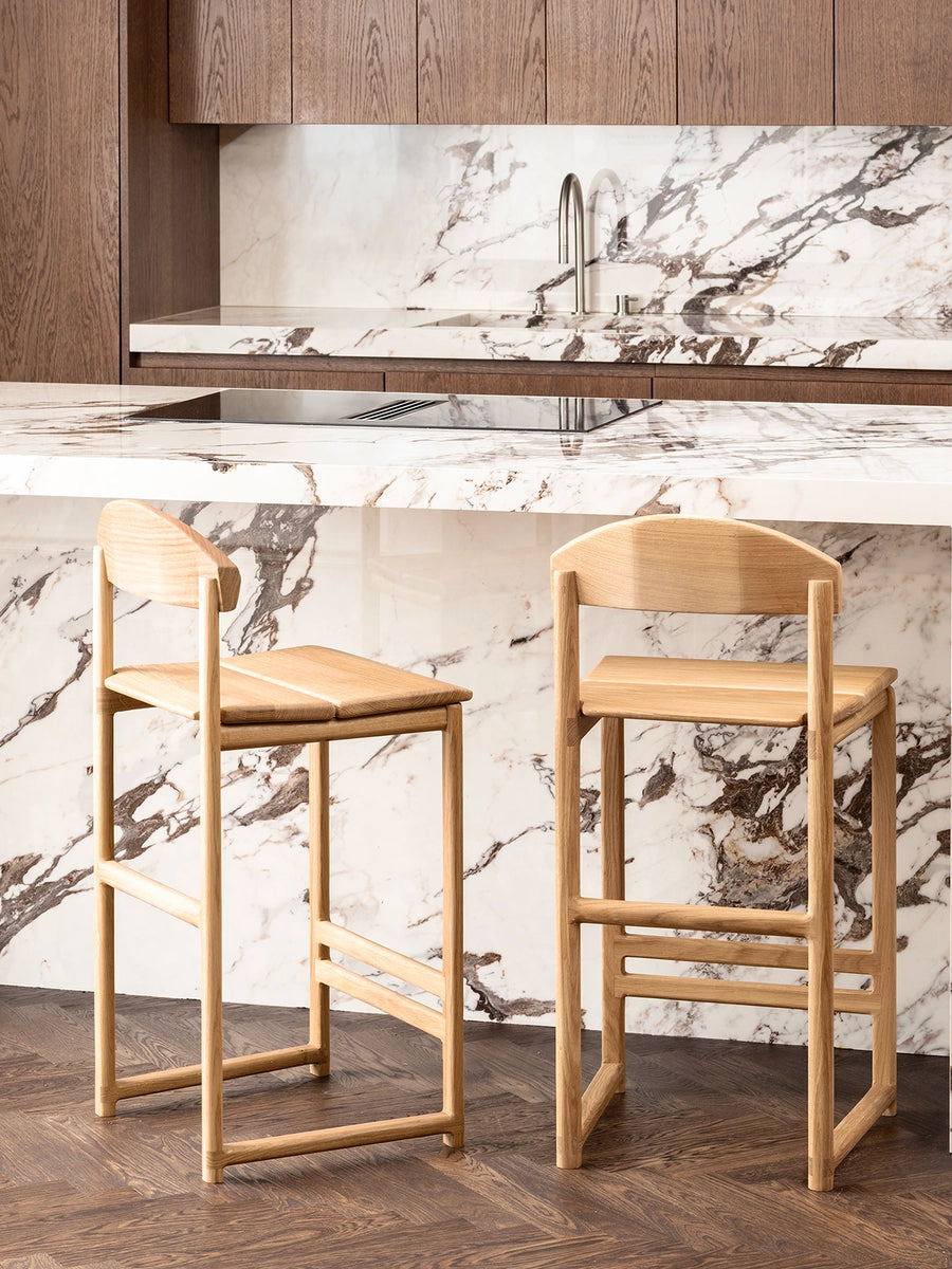Oak Bar Stool Ted in a modern kitchen with a marble countertop and wooden cabinetry.