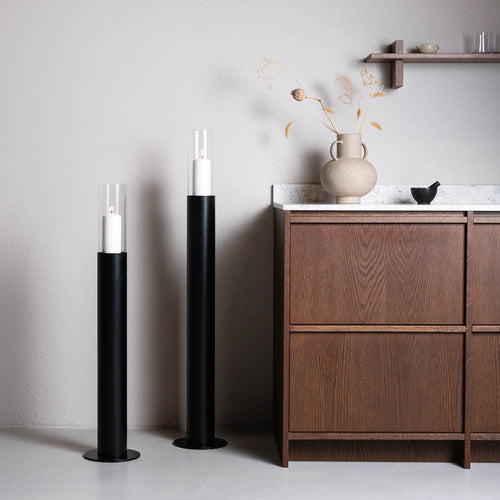Pair of black Thomas candle holders with glass hurricane tops, placed beside a dark oak cabinet with Caesarstone countertop in a Scandinavian interior.