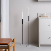 Pair of tall Vera candle holders in black with Caesarstone base, styled in a minimalist interior next to a white kitchen cabinet and oak furniture.