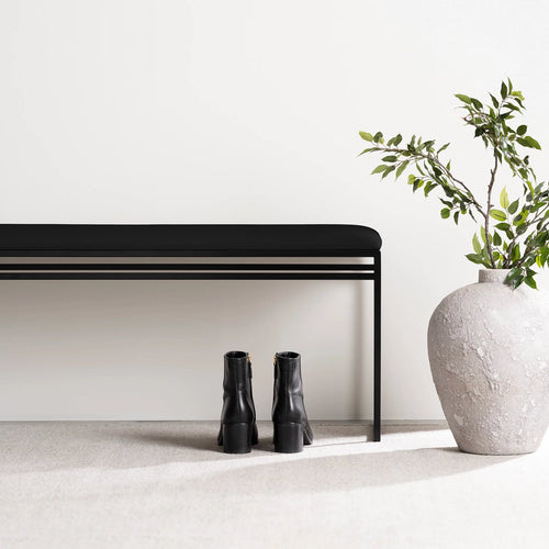Wilma bench in black with vegan leather seat, minimalist design, with black boots and a plant beside it.