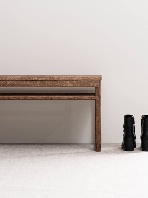 Oak Bench in dark oak frame beside black boots on a neutral background, perfect for hallways or entryways.