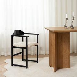 Erik chair in black oak with ivory bouclé seat next to the Ann dining table in solid oak, set in a minimalist dining room with soft natural light and sculptural candleholders.