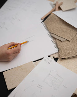 Close-up of the design process at by Crea, featuring hand-drawn furniture sketches, fabric swatches in neutral tones, Dekton stone samples, and a designer