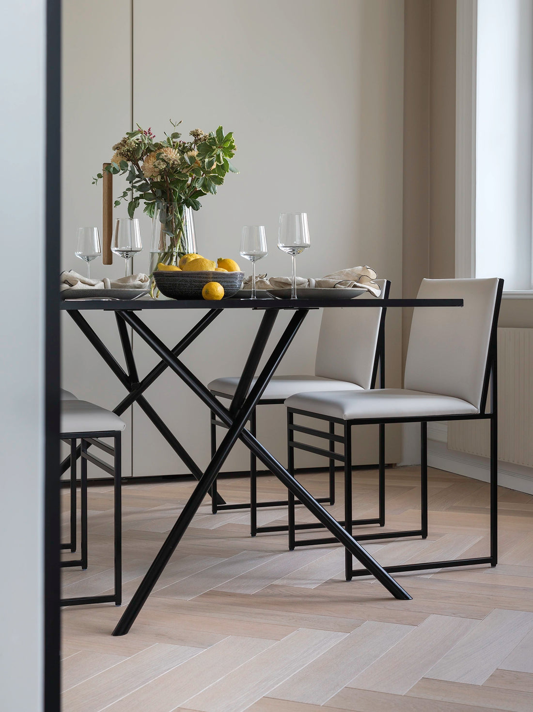 Dining Chair Isabell in ivory vegan leather around a black metal dining table, styled with flowers and fruit