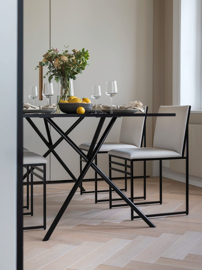 Dining Chair Isabell in ivory vegan leather around a black metal dining table, styled with flowers and fruit