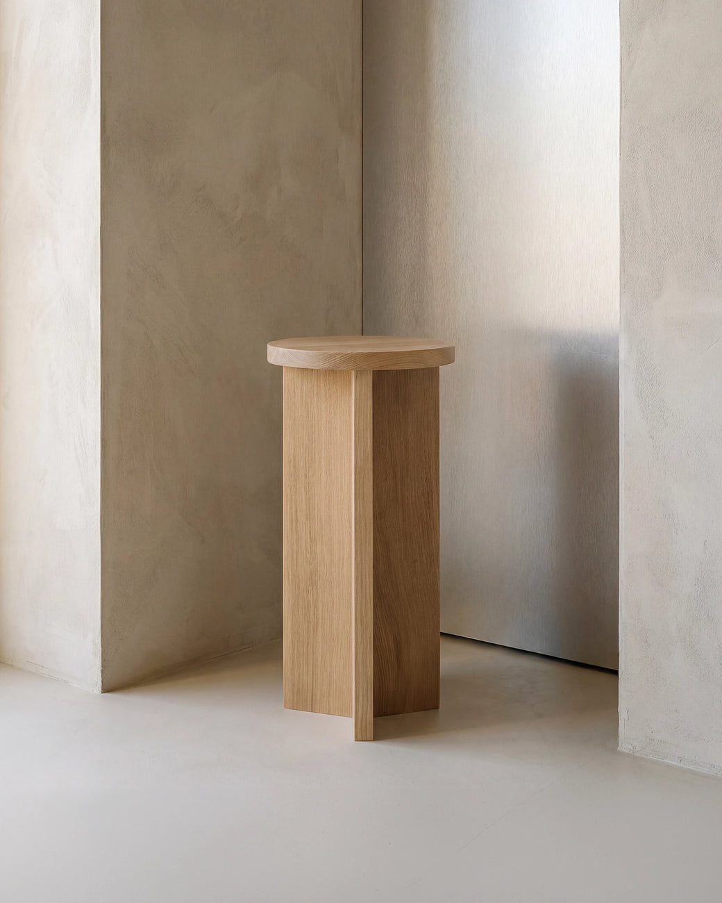 Affe pedestal in solid oak with a round top and sculptural base, styled in a minimalist Scandinavian interior with soft neutral walls and natural light.