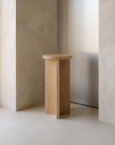 Affe pedestal in solid oak with a round top and sculptural base, styled in a minimalist Scandinavian interior with soft neutral walls and natural light.