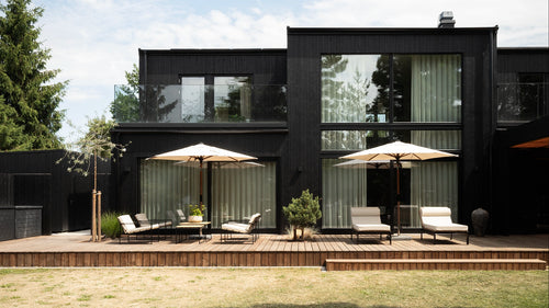 The garden facade of the black timber villa in Höllviken, with the Arvid lounge group and Bazo sun loungers arranged as outdoor rooms along the deck.