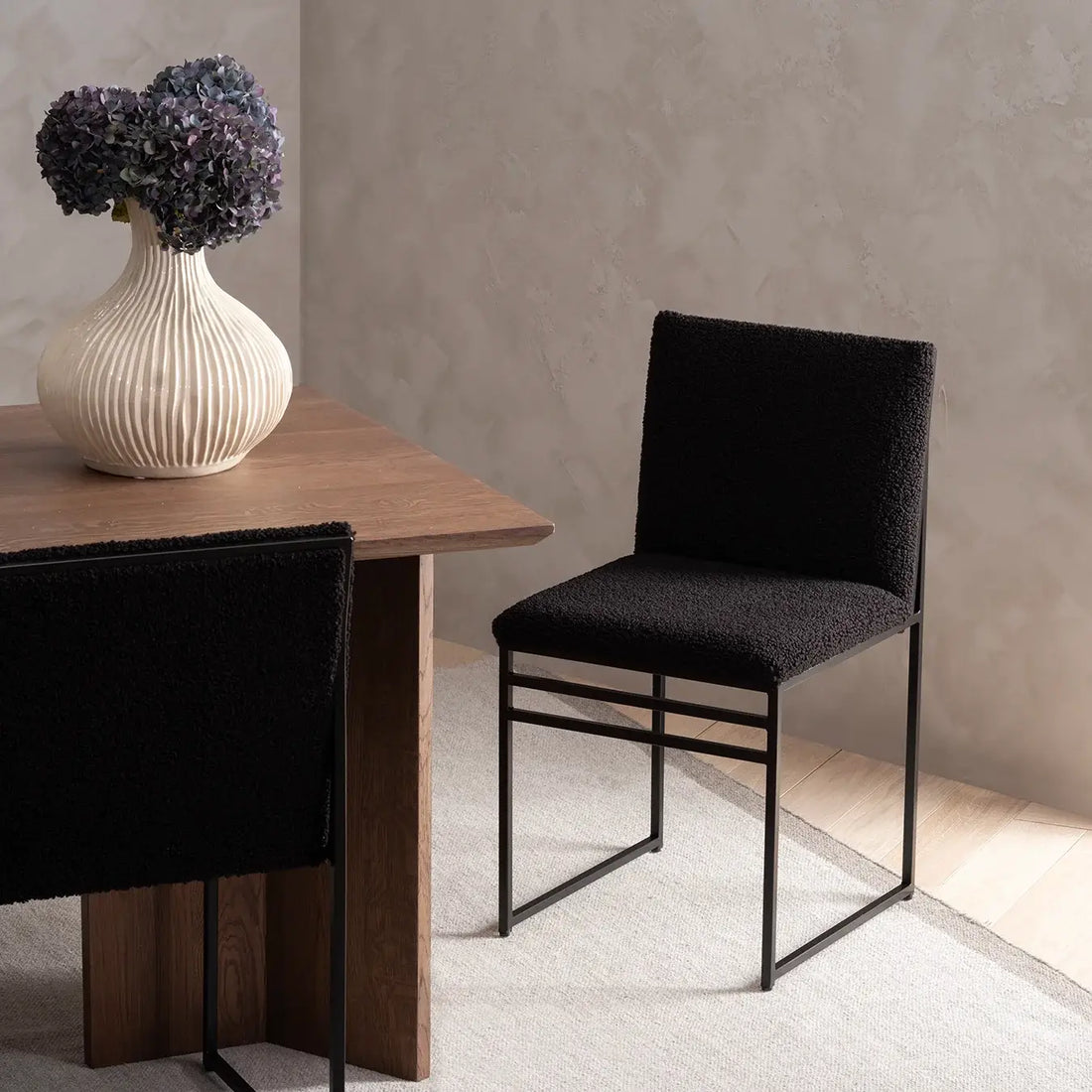 Dining chair Isabell with black frame and bouclé cushion in a stylish dining room setting.