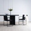 Ann dining table in black oak with two modern chairs and a vase of flowers in a minimalist setting.